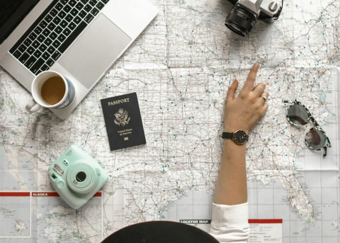Hand on map with camera, passport, laptop, and coffee, perfect for travel planning inspiration.