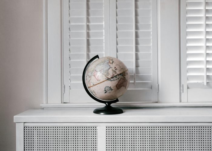 Elegant globe on a minimalist white desk against shuttered windows in modern interior design.